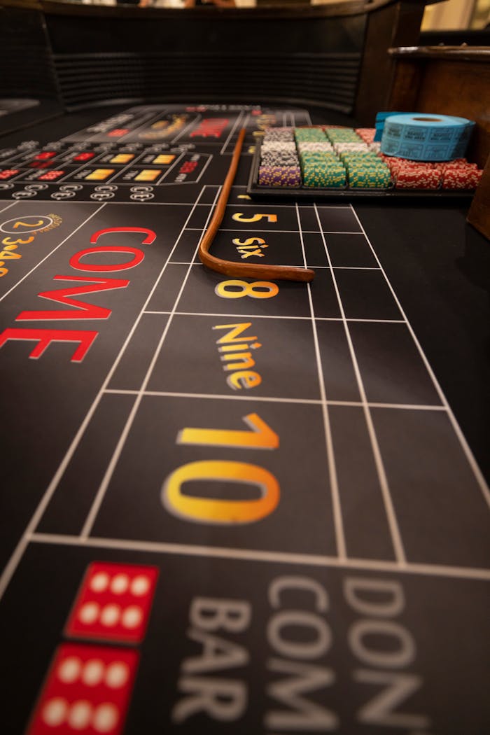 Close-up of a craps table in a casino, showing betting lines, poker chips, and wooden stick.