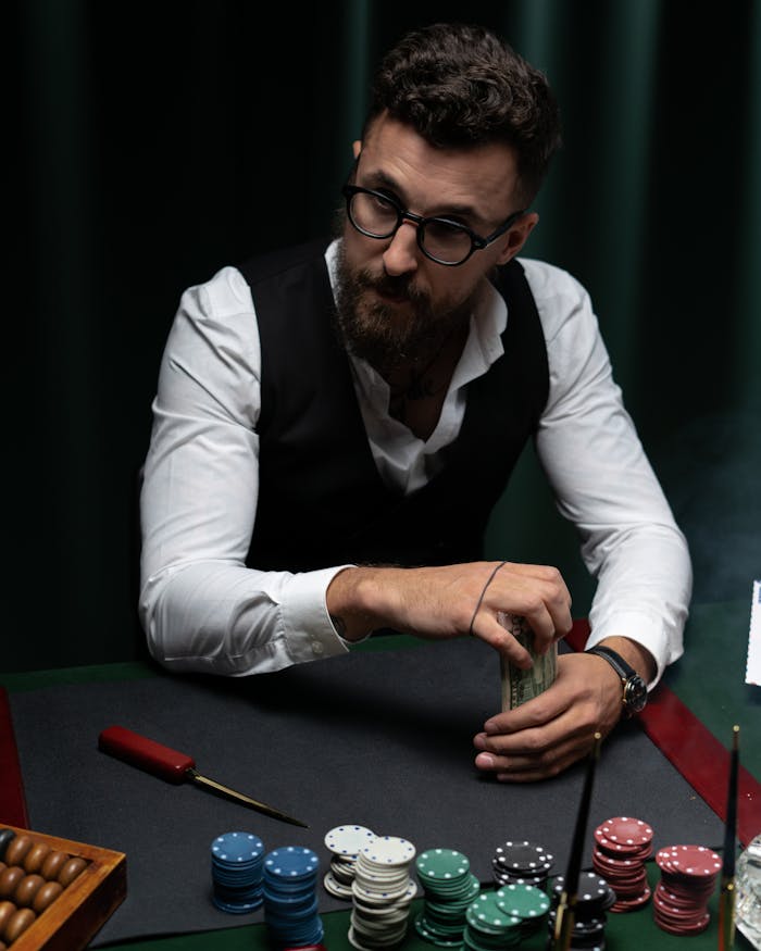 about-01 A bearded man with glasses plays poker, strategizing with a stack of chips.