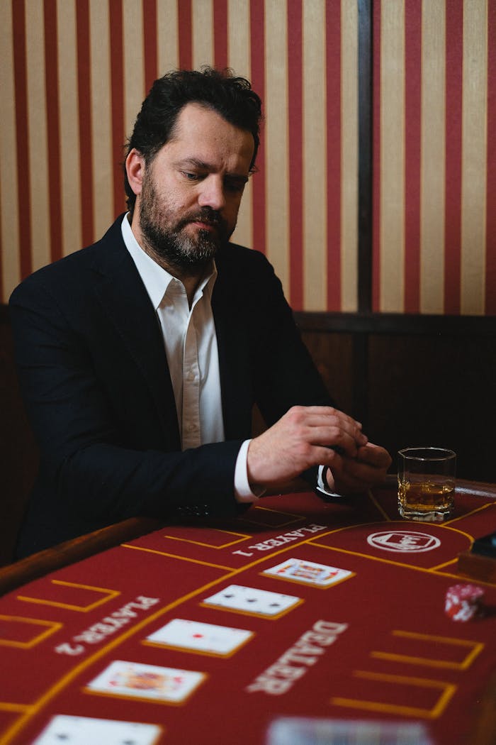 services-hero Adult man in a suit playing cards at a casino table with a drink, pondering his next move.